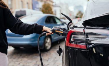 Woman near car. Vehicle charged at the charging station.